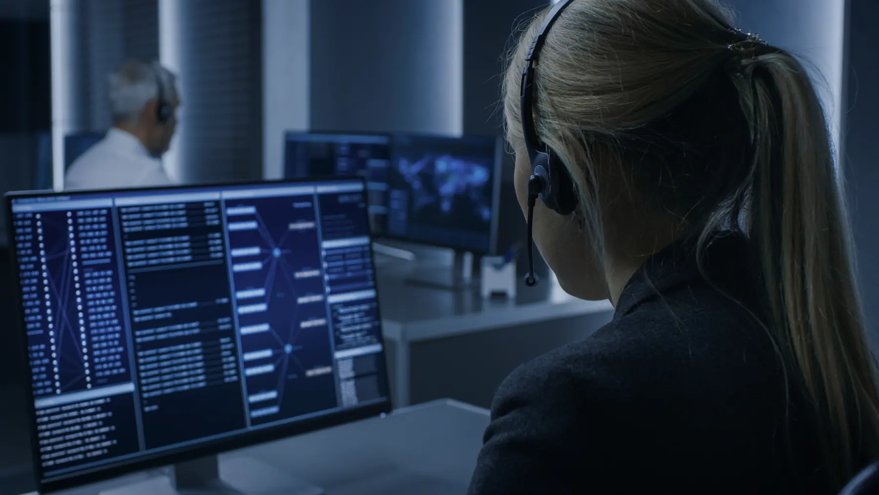 Technician with a headset in front of several monitors in a control room