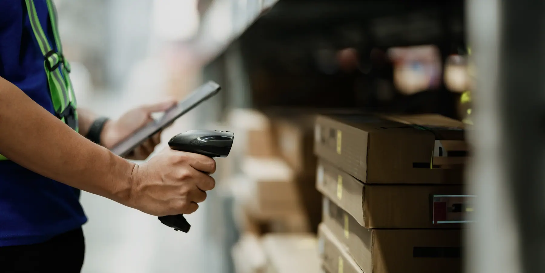 Hand holding a barcode scanner in front of boxes in a warehouse